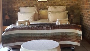 A room with a bed, pillows, a round table, and a brick wall. - Roaring Sky (Cullinan)