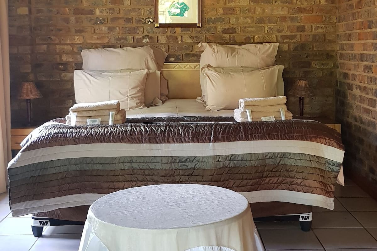 Um quarto com cama, almofadas, uma mesa redonda e uma parede de tijolos.