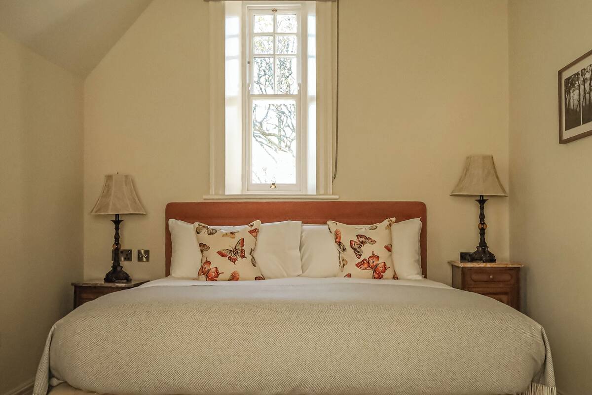 A bedroom with a large bed, two nightstands, a window, and a wall-mounted picture.