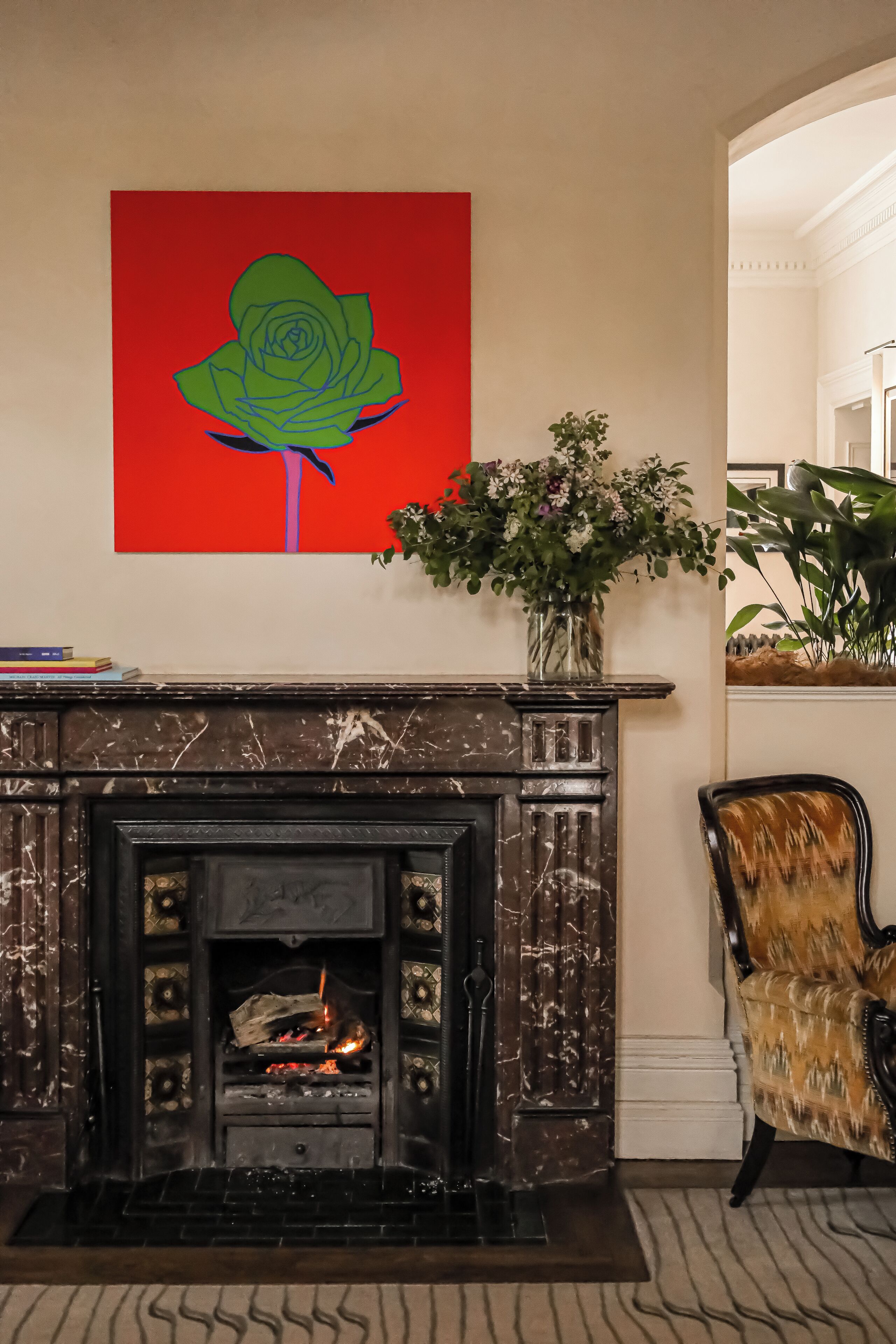 A fireplace with a modern design, a vibrant abstract painting above it, and a potted plant beside the fireplace.