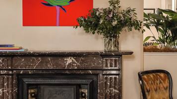 A fireplace with a modern design, a vibrant abstract painting above it, and a potted plant beside the fireplace.