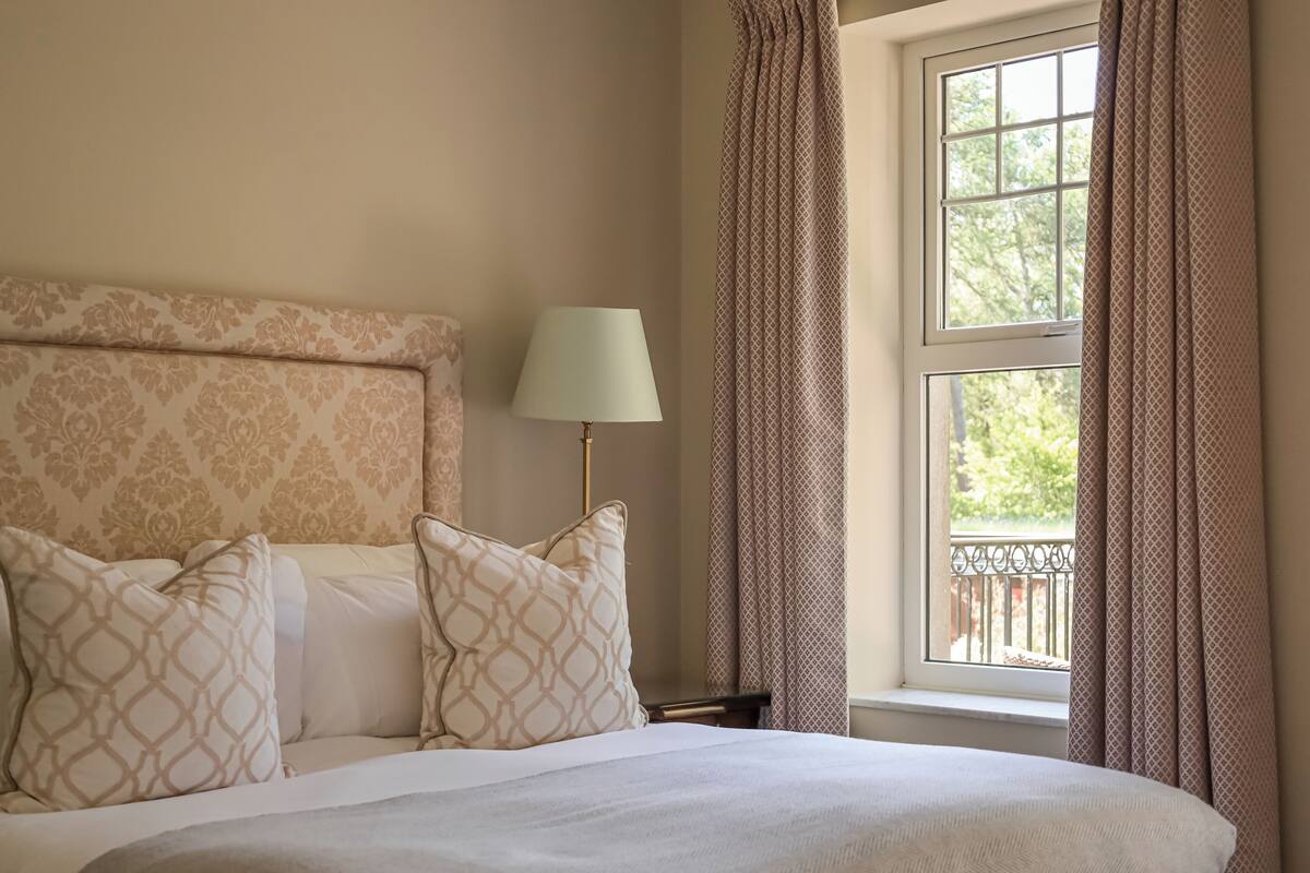 A neatly made bed with patterned pillows, a bedside lamp, and a window with curtains.