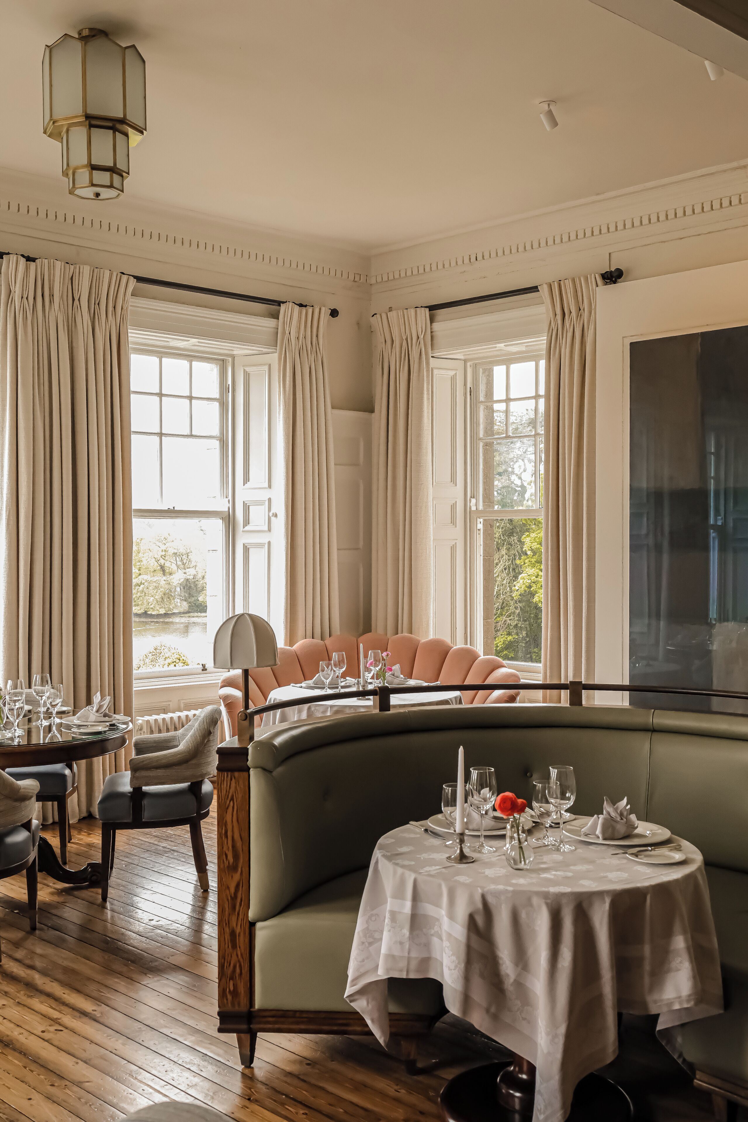 A dining area with a round table set for two, a cushioned bench, and a view of the outdoors through large windows.