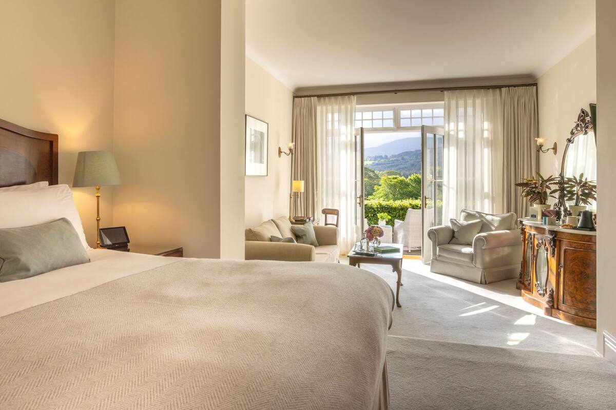 A hotel room with a large bed, a desk, two armchairs, a sofa, and a view of the outdoors.