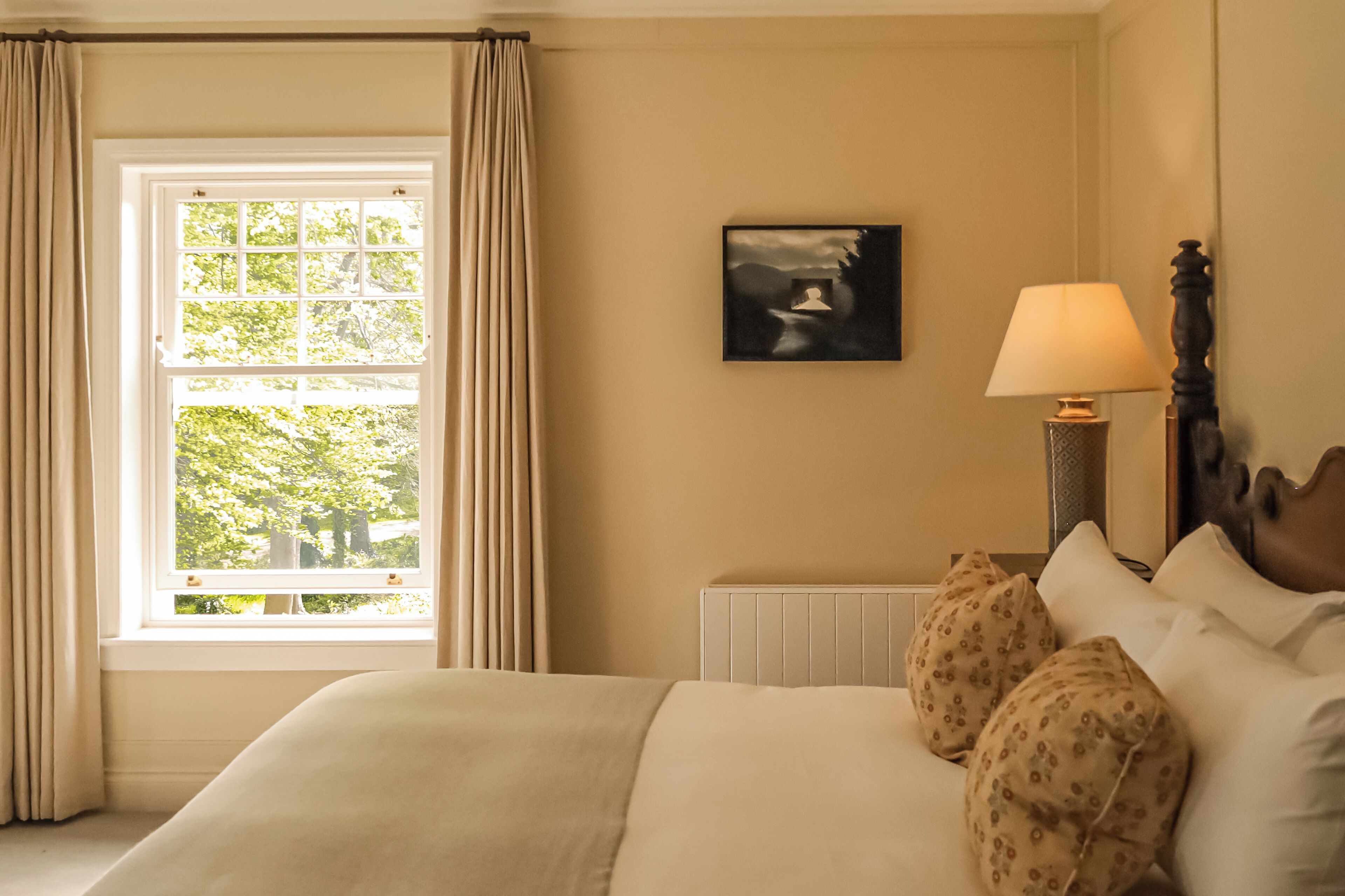 Een slaapkamer met een groot raam, een bedlampje en een lijst met een afbeelding aan de muur.