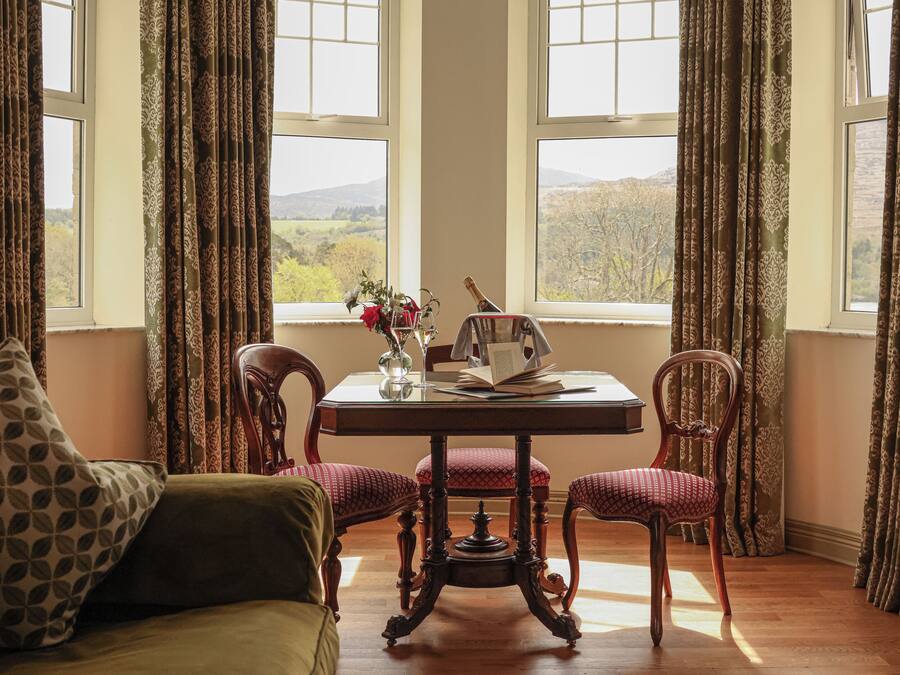 Una habitación con una mesa de madera, dos sillas, un sofá y vistas al campo a través de amplias ventanas.