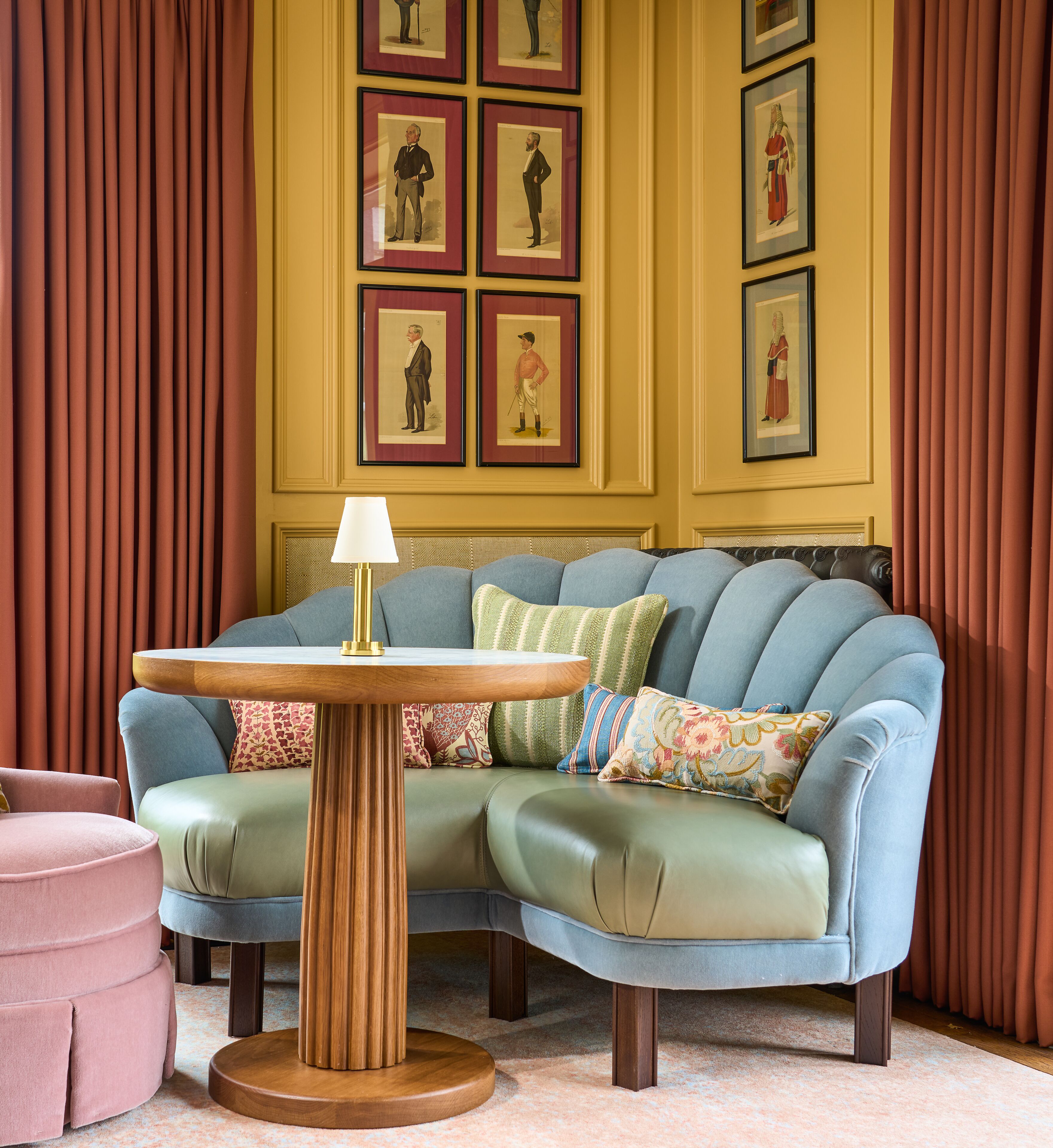 A room with a blue sofa, a wooden table with a lamp, and framed pictures on the wall.