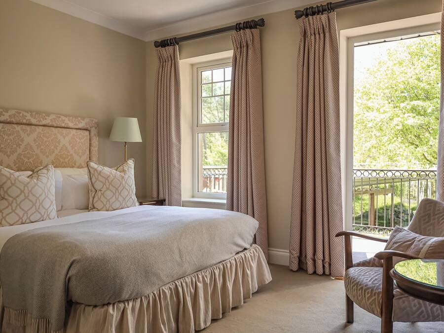 A bedroom with a large bed, a chair, and a window with curtains.