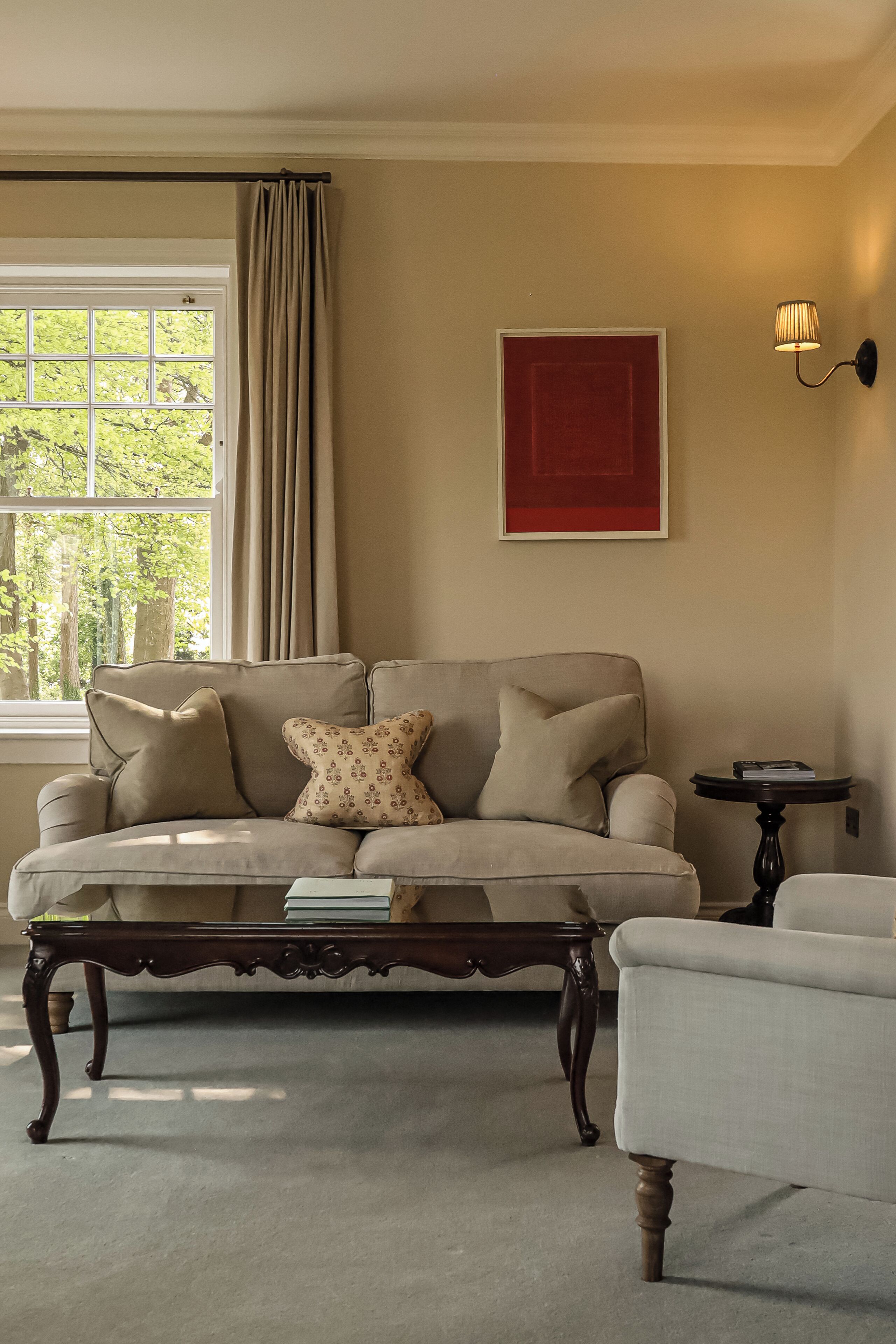A living room with a beige sofa, a wooden coffee table, a small side table, and a red abstract painting on the wall.
