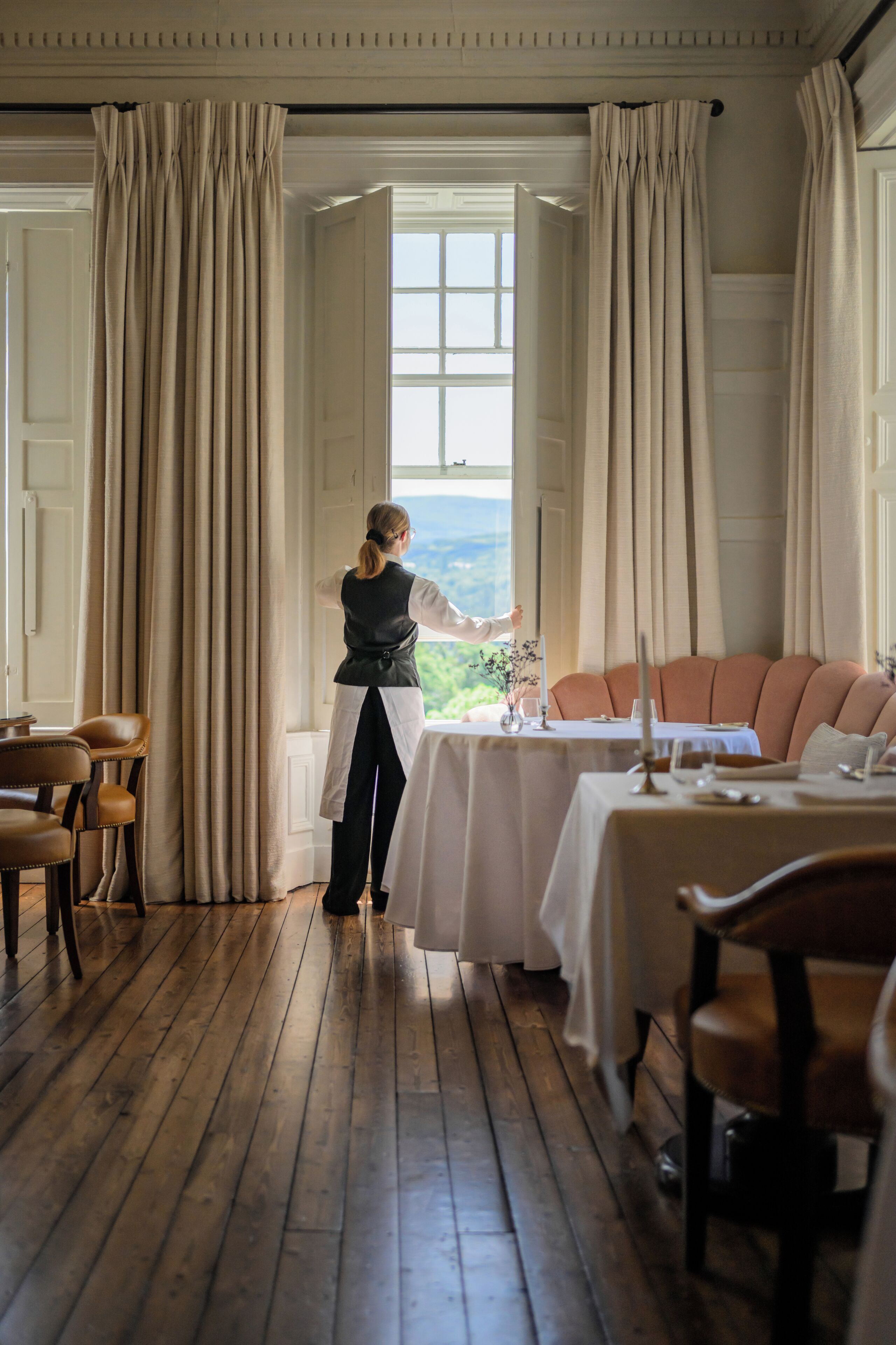 A hotel room with a large window, a dining table set for two, and a sofa.