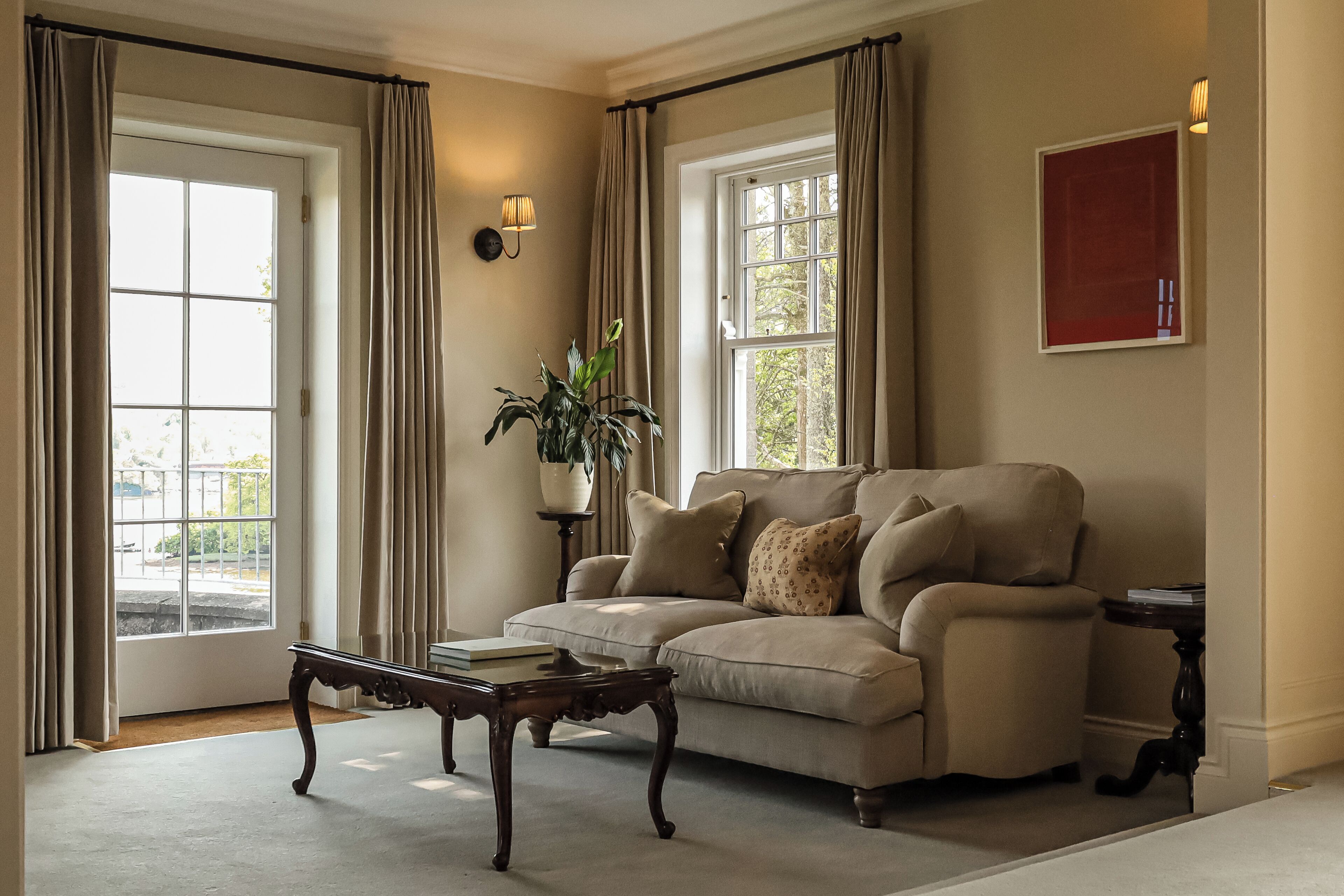 A living room with a beige sofa, a wooden coffee table, a potted plant, and a wall-mounted lamp.