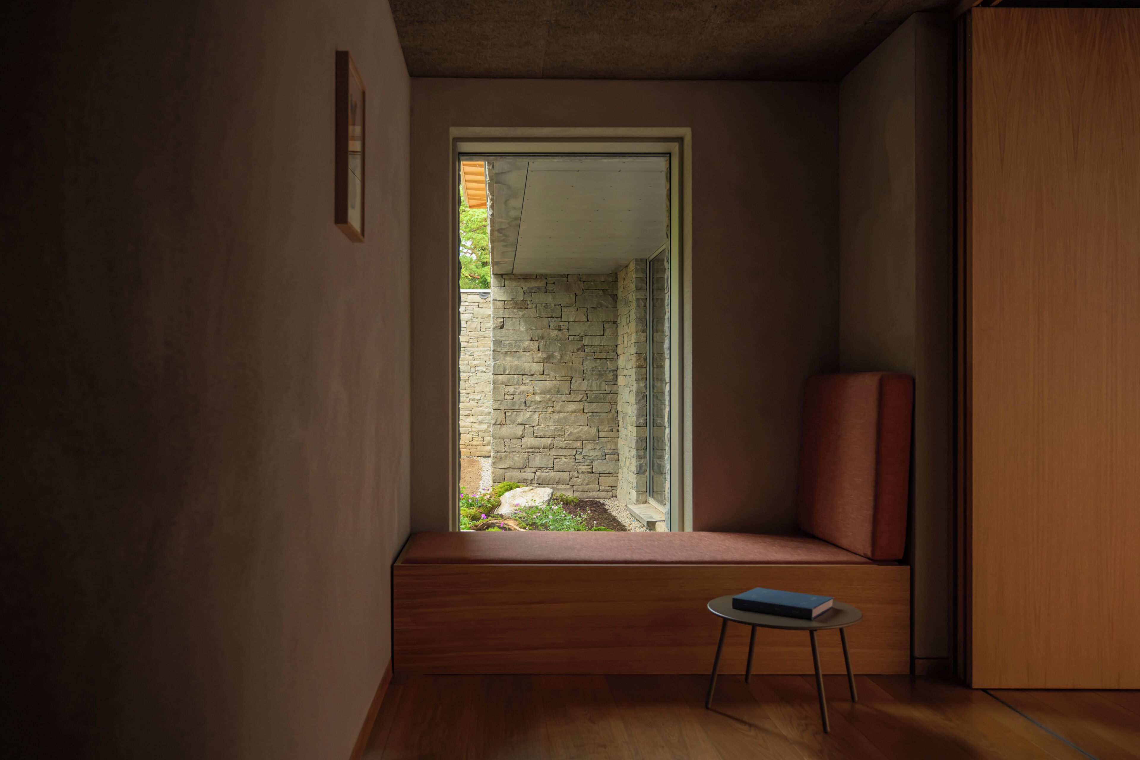 Un interior moderno con un banco empotrado, una mesita y vistas a una pared de piedra y vegetación.