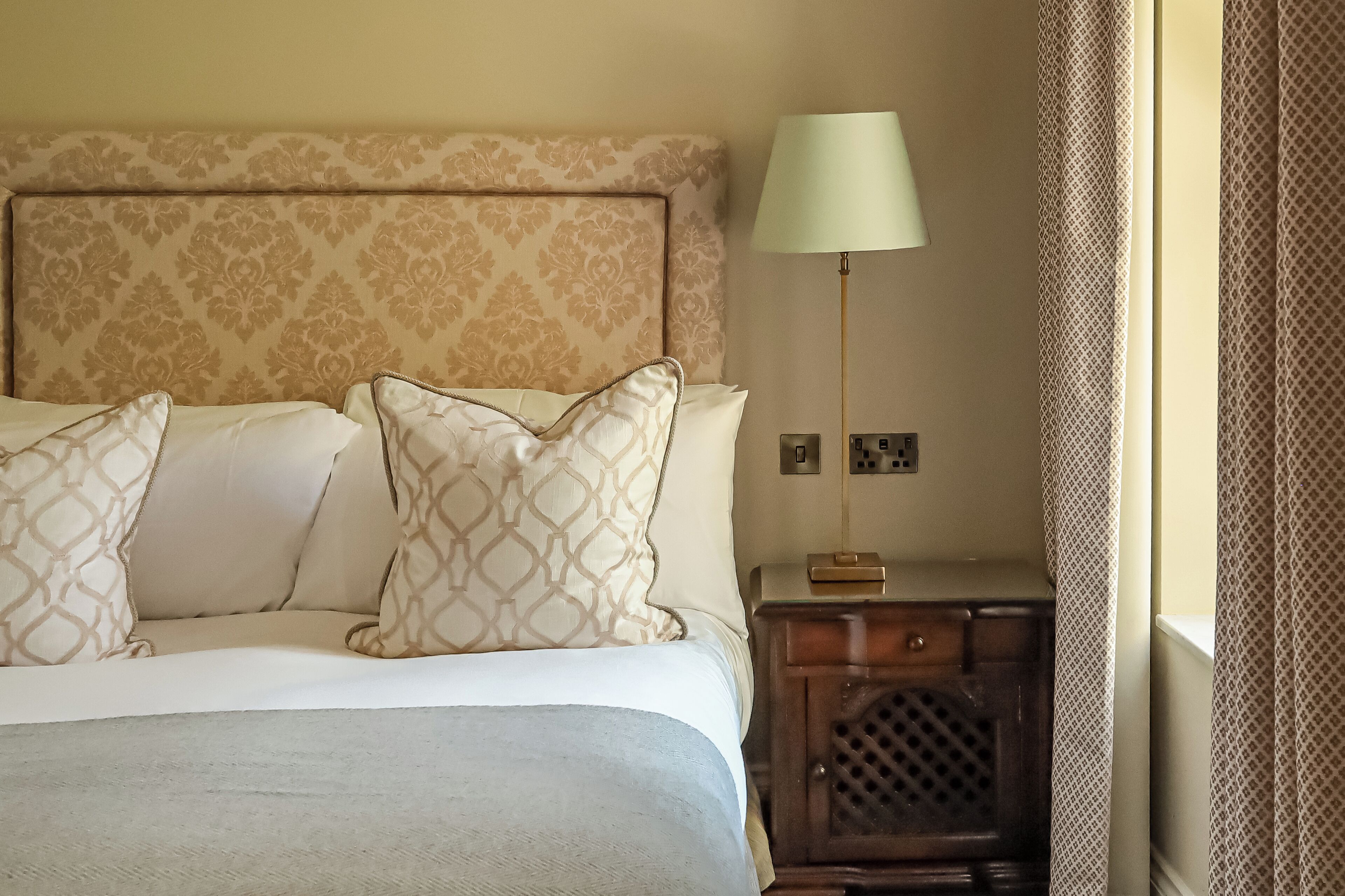 A neatly made bed with patterned pillows, a bedside lamp, and a small wooden nightstand with a drawer.