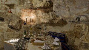 A stone-walled room with a table set for a meal, candles, and a bottle of wine. - L'Auberge De Tamezret (Matmata)