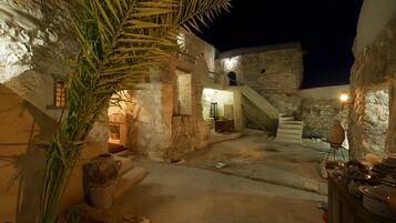 Un patio tenuemente iluminado con muros de piedra, una palmera y una escalera que conduce a un nivel superior.