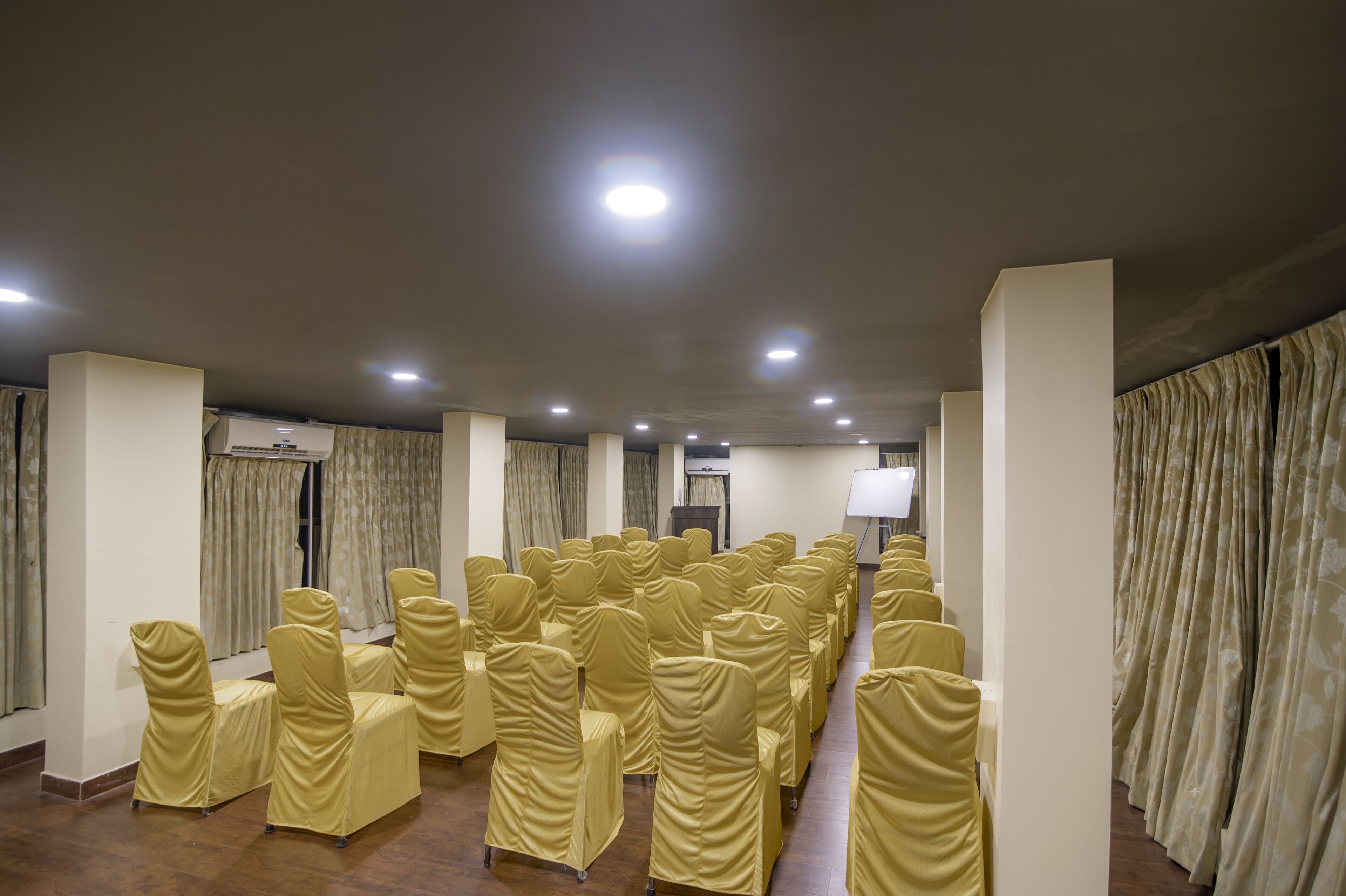 A conference room with rows of chairs covered in yellow fabric, a whiteboard, and a projector screen.