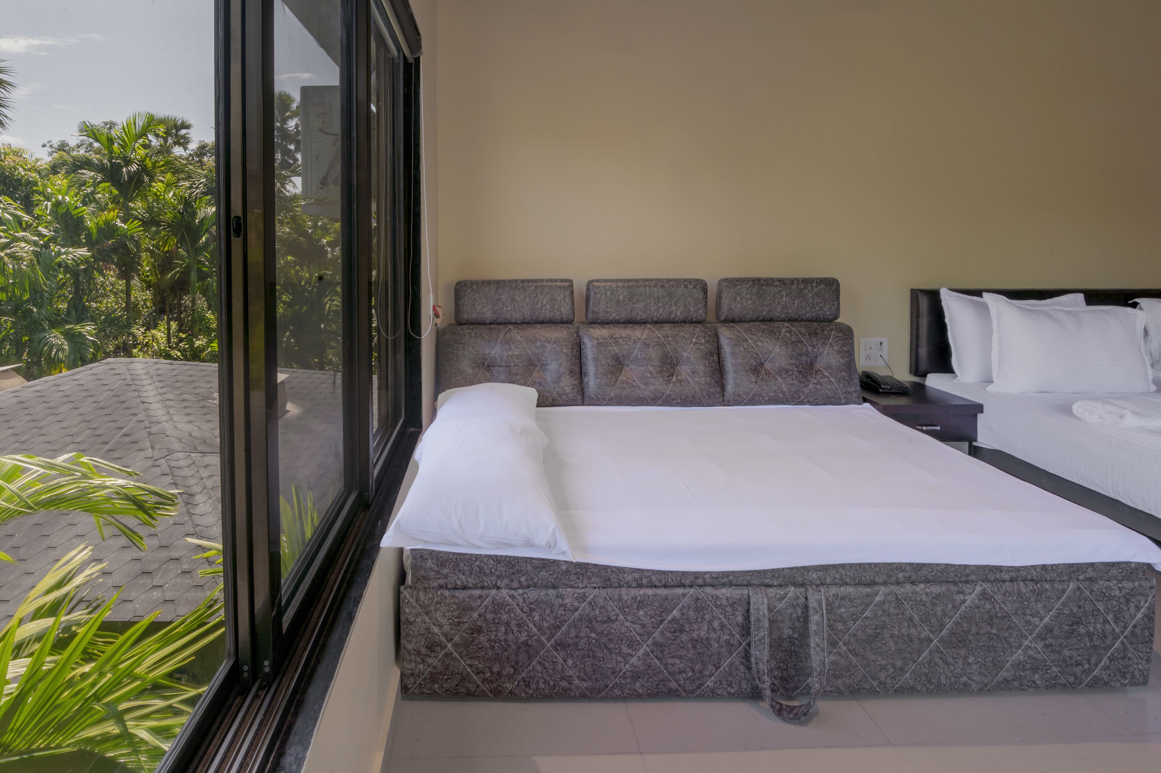 Een moderne hotelkamer met een groot bed, een nachtkastje en uitzicht op weelderige begroeiing door een groot raam.