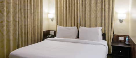 A hotel room with a large bed, two bedside tables, and curtains.