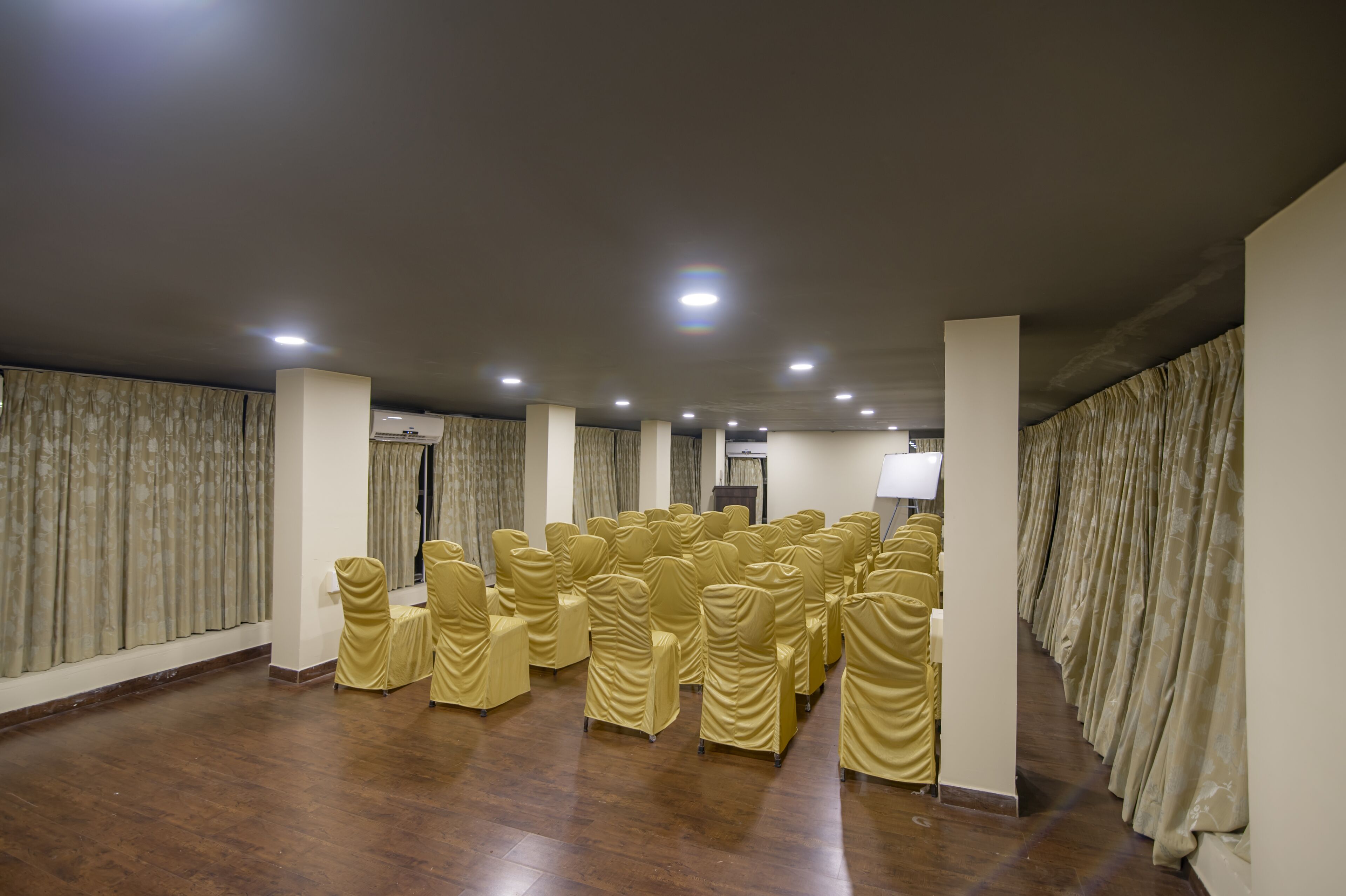 A conference room with rows of chairs covered in yellow fabric, a white air conditioning unit, and a white lamp on a stand.