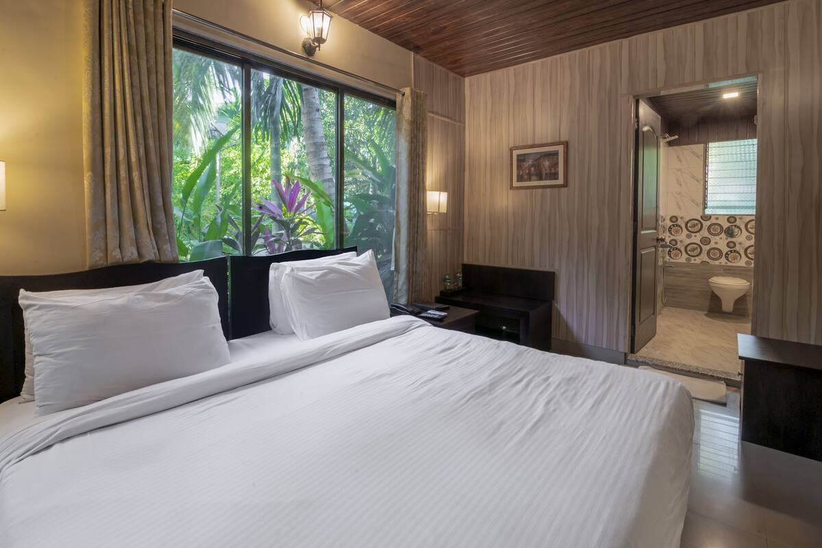 Une chambre d’hôtel avec un grand lit, une table de chevet, une télévision et une salle de bain visible à travers une porte ouverte.