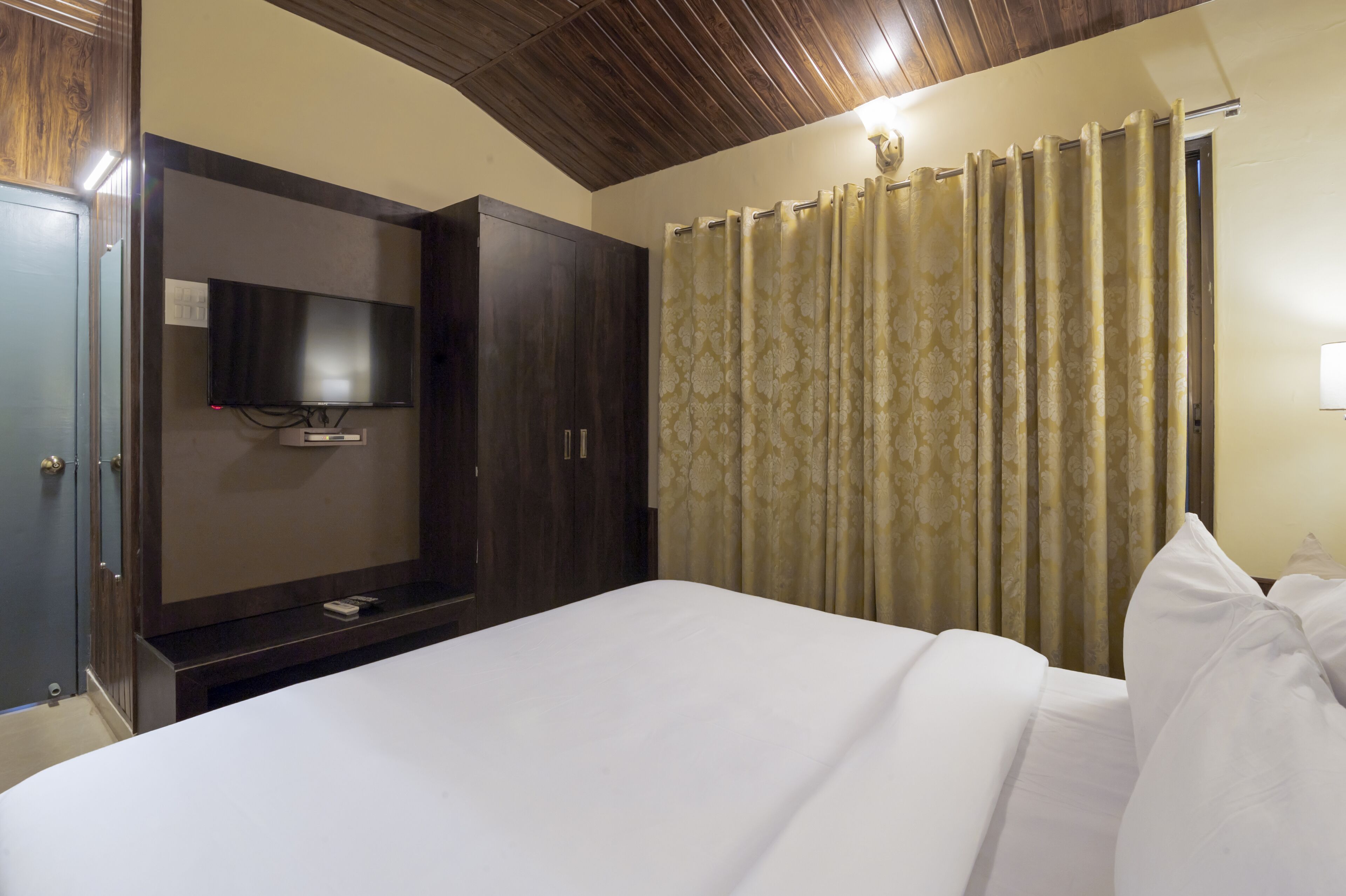 A hotel room with a bed, a television mounted on a wooden cabinet, and a curtain with a floral pattern.
