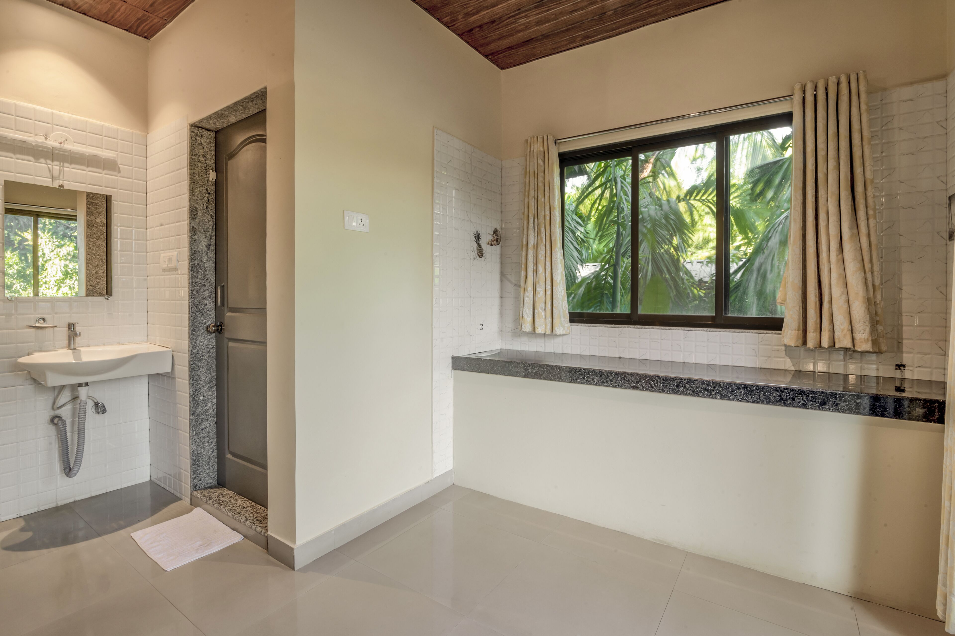 A bathroom with a sink, shower, and window with curtains.