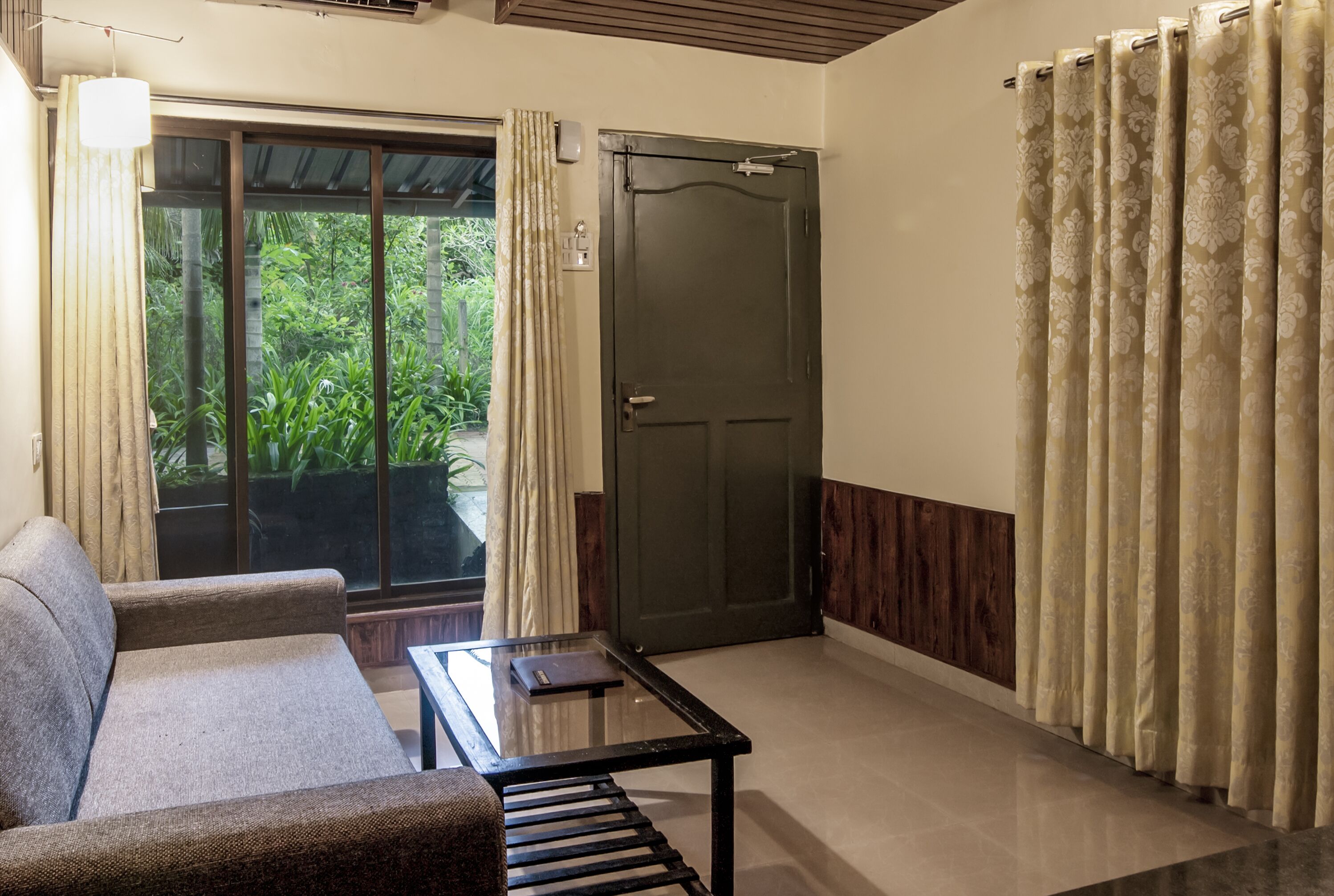 A room with a sofa, a glass-top table, a door, and curtains.