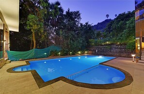 A swimming pool with a unique shape, surrounded by a stone wall and lush greenery. - Silvanus Forest Retreat (Alibag)