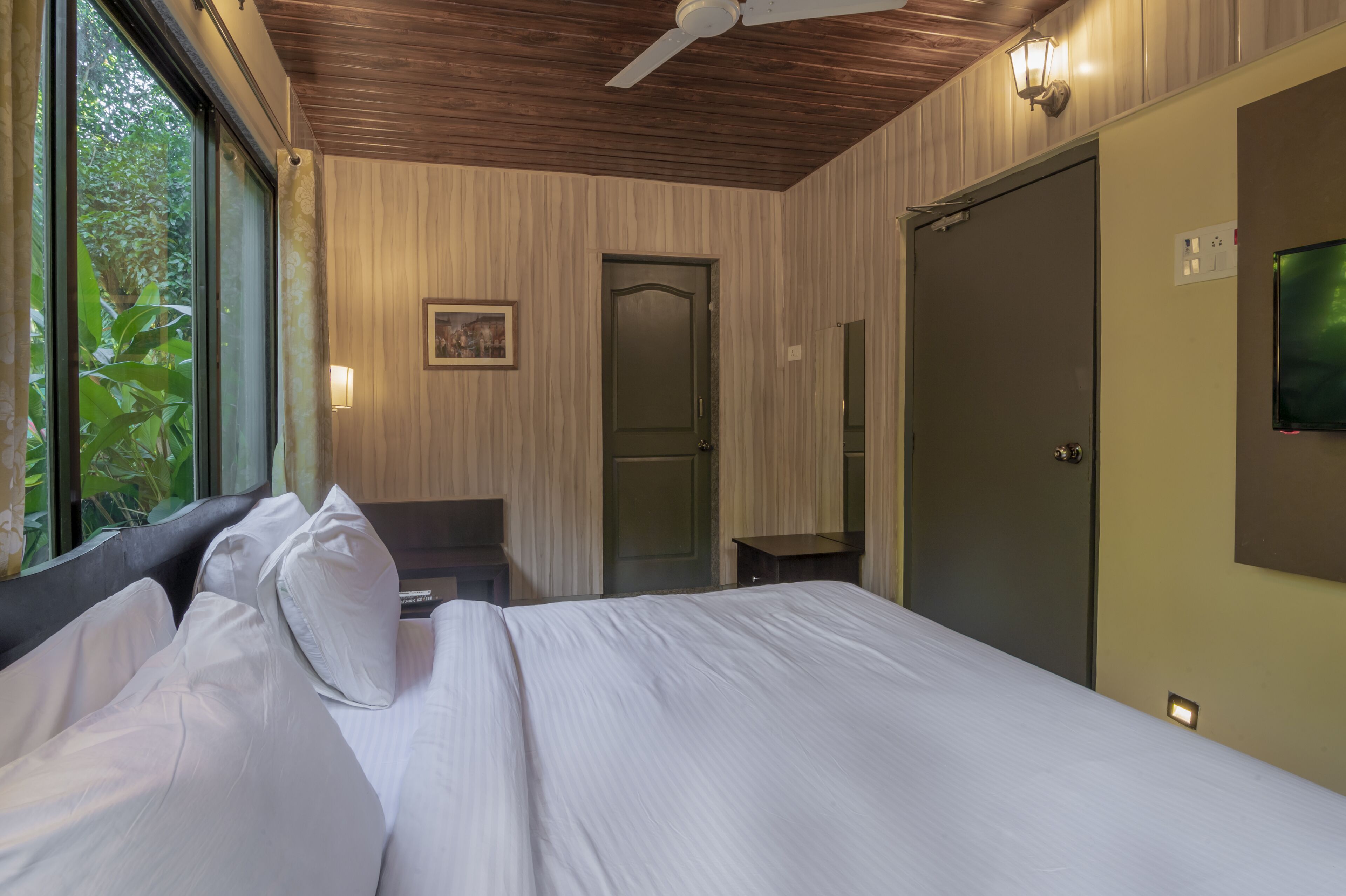 Ein Schlafzimmer mit Bett, Schreibtisch, Stuhl, einer Tür und einem Fenster mit Vorhängen.