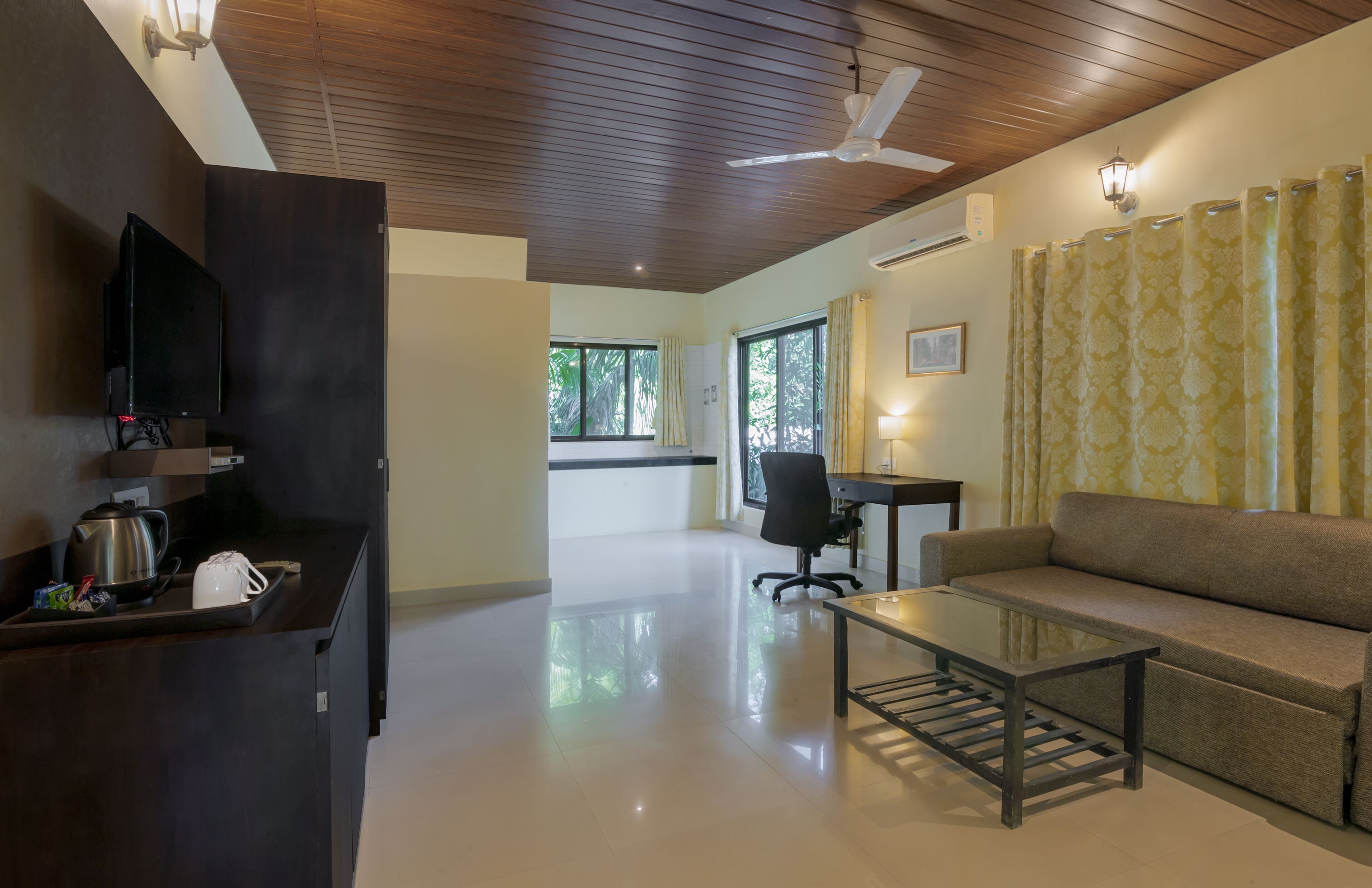 A modern living room with a sofa, a glass coffee table, a TV, and a kitchen area with a kettle and toaster.