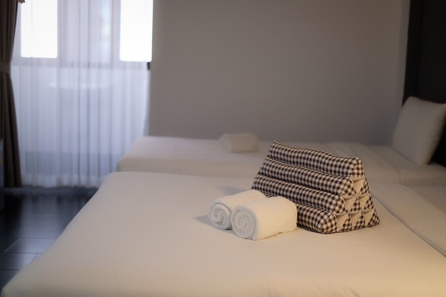 A hotel room with two beds, each with a white mattress and a checkered pillow.