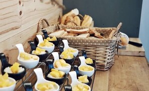 A table with bowls of a yellow dessert, a wicker basket with bread, and a wooden wall. - Shane Hotel Chiangmai (Chiang Mai)
