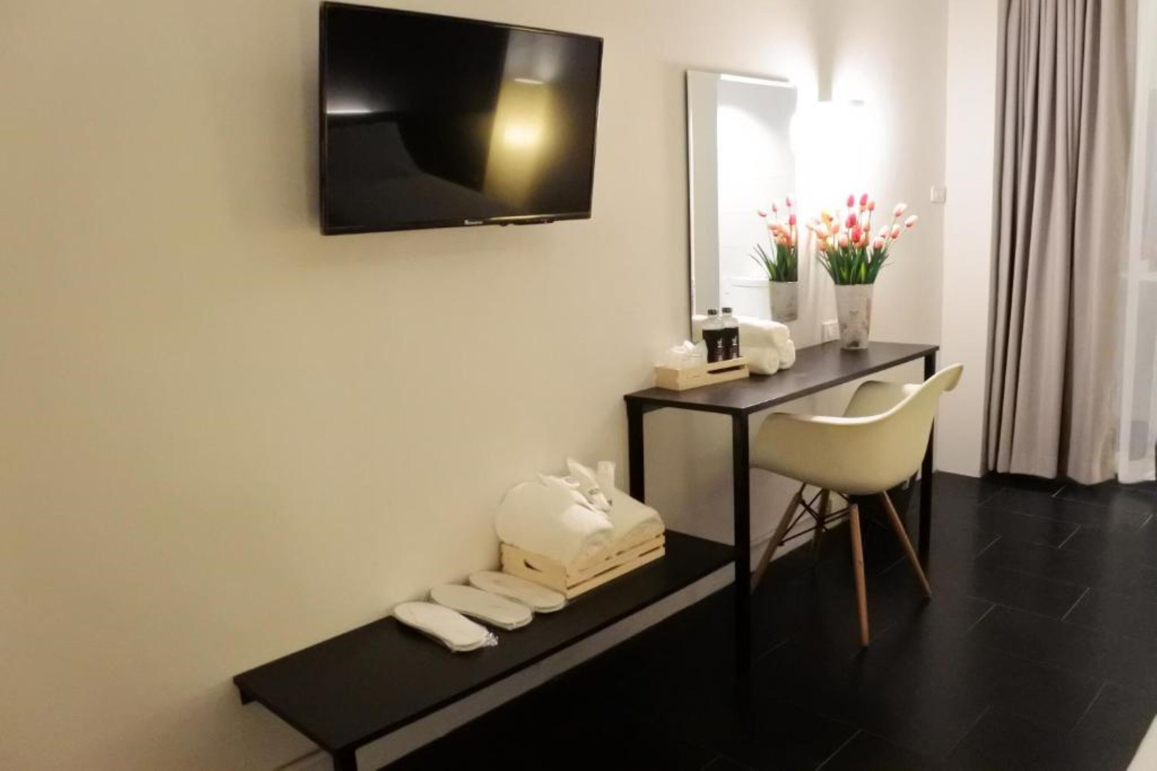 Una habitación de hotel moderna con una televisión de pantalla plana montada en la pared, una mesita con un florero, un banco con toallas y una silla.