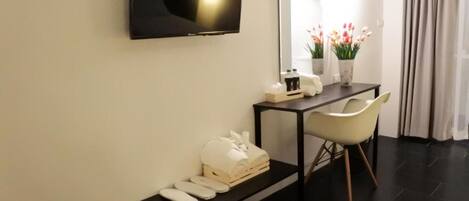 Una habitación de hotel moderna con una televisión de pantalla plana montada en la pared, una mesita con un florero, un banco con toallas y una silla.