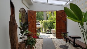 A pathway leading to an outdoor seating area with a wooden bench and a table, surrounded by potted plants and a white wall. - Shane Hotel Chiangmai (Chiang Mai)