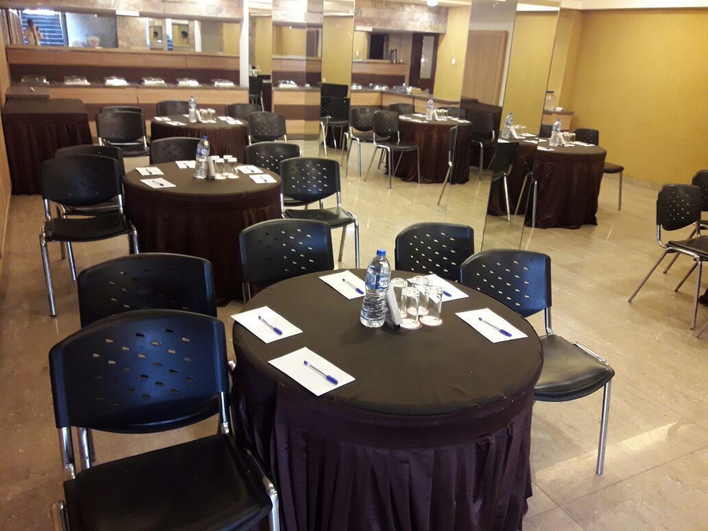 Une salle de conférence avec des tables rondes, des chaises noires et des bouteilles d’eau.