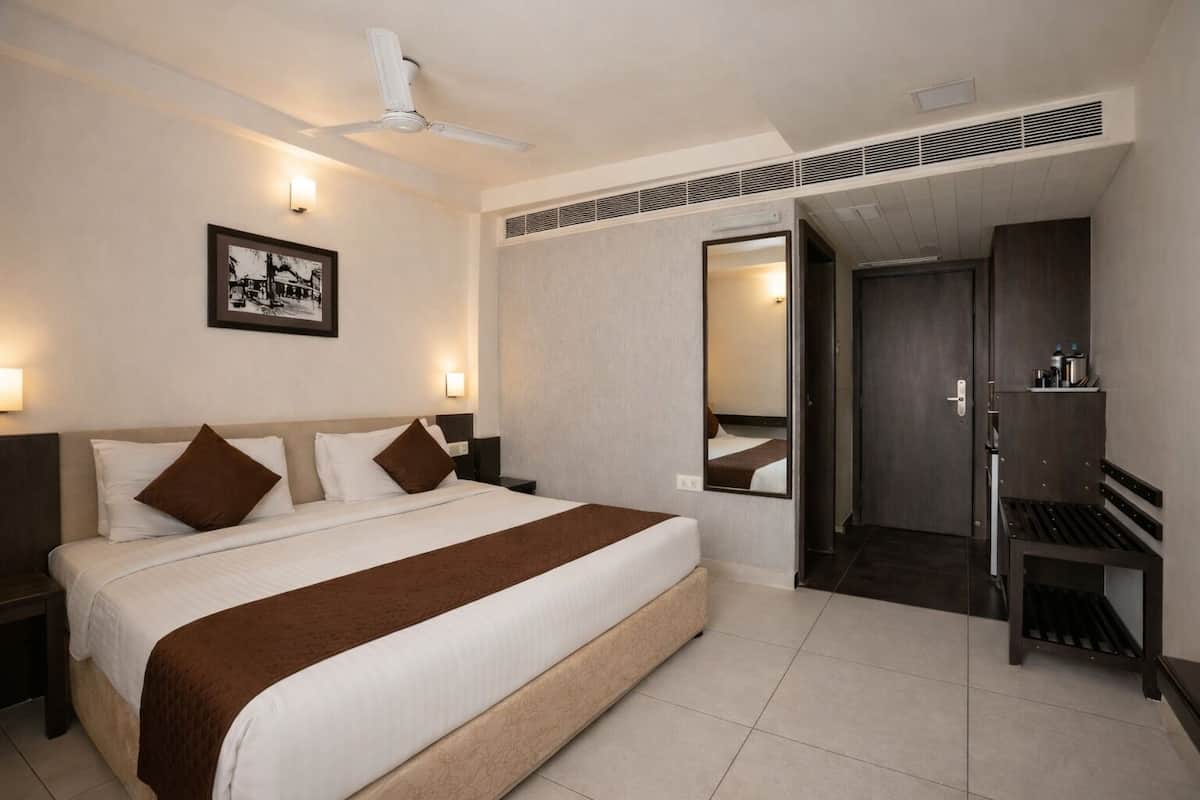 Ein Hotelzimmer mit Bett, Nachttischen, Deckenventilator, Spiegel, Kleiderschrank und einer Tür zu einem anderen Raum.