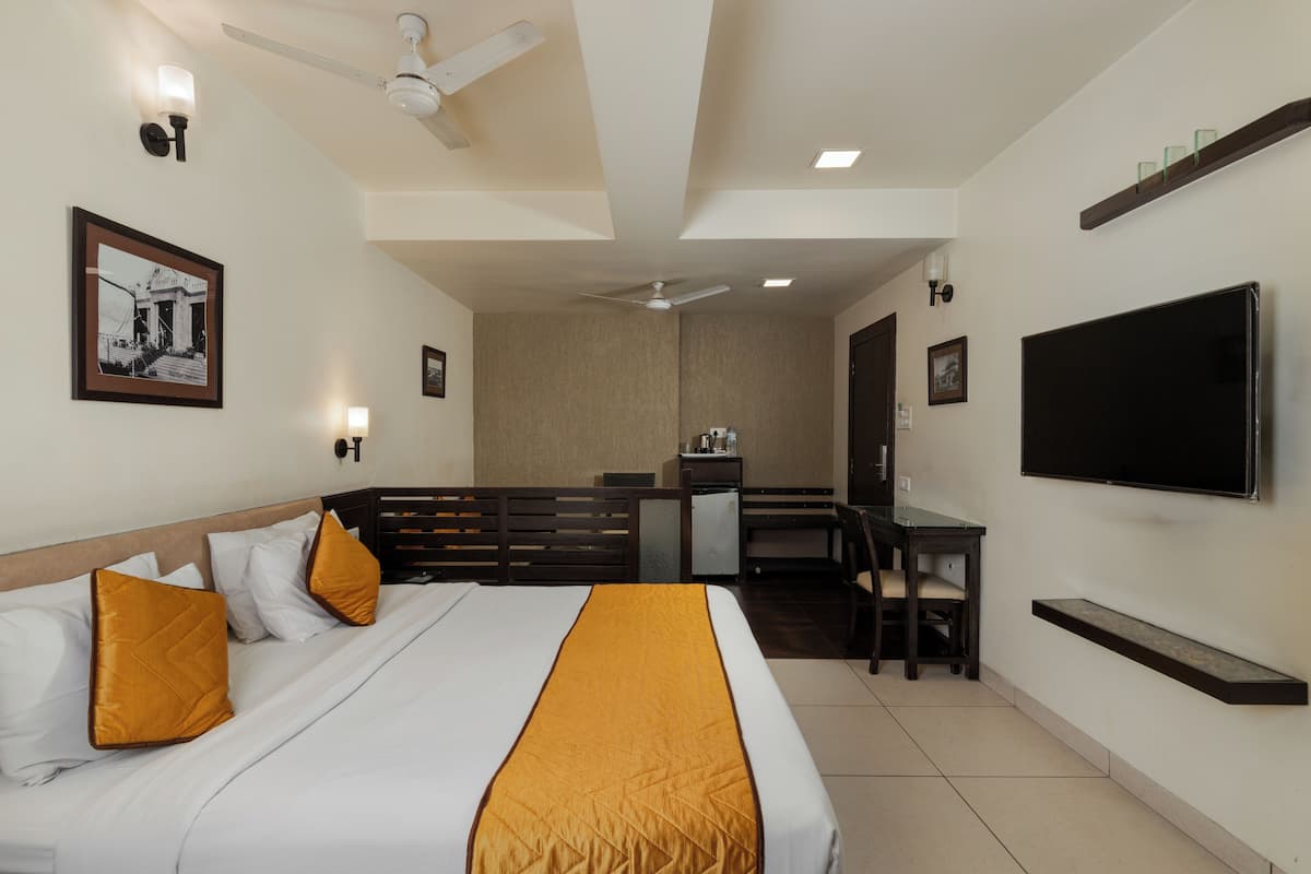 Ein Hotelzimmer mit Bett, Schreibtisch, Stuhl, Fernseher und Deckenventilator.