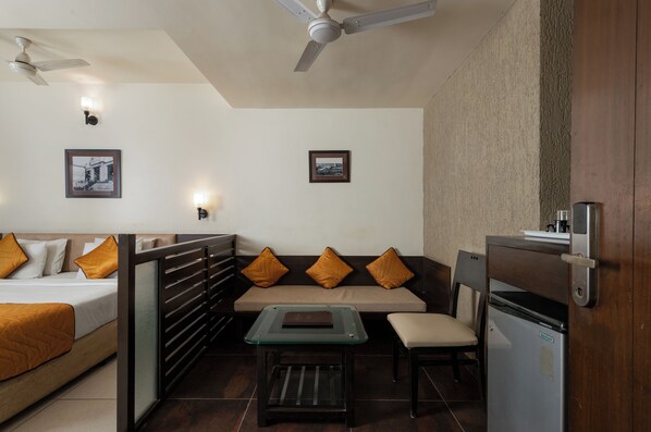 Habitación de hotel con cama, sofá, mesita y refrigerador.
