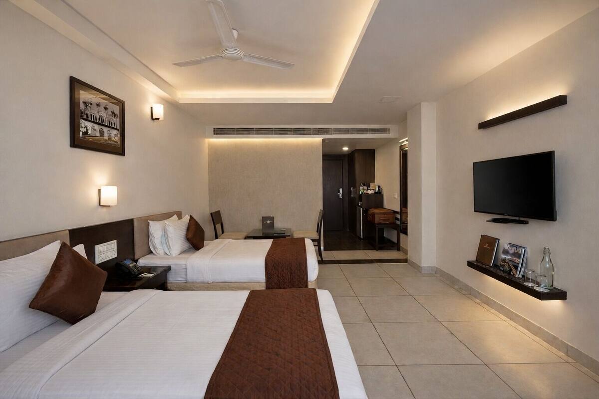 Ein Hotelzimmer mit zwei Betten, einem Fernseher, einem Deckenventilator und einer kleinen Küchenzeile.