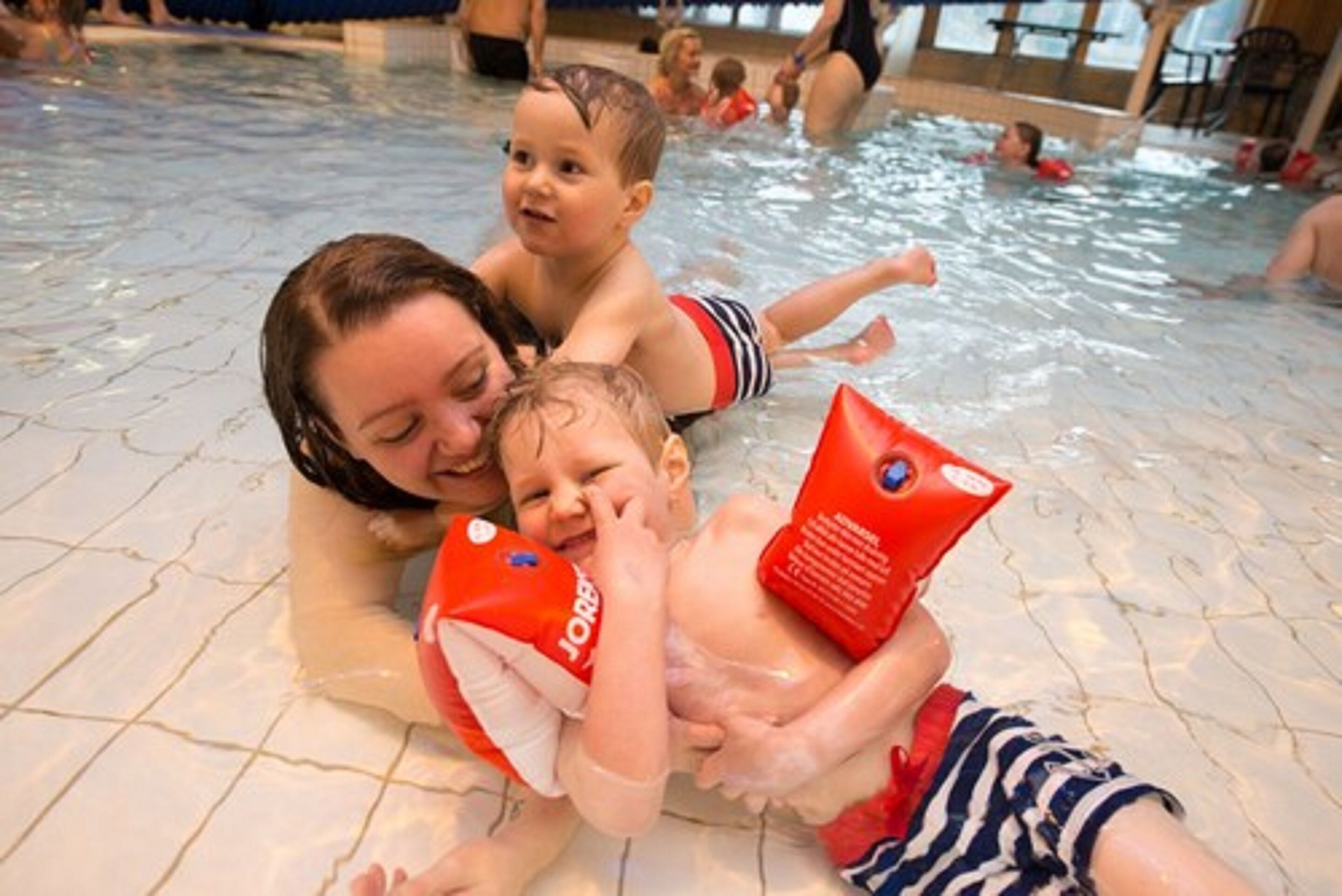 A pool area with people swimming and a child holding a red object.