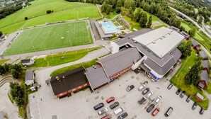 Eine Vogelperspektive eines Sportkomplexes mit einem Fußballplatz, einem Schwimmbecken und einem großen Gebäude mit Parkplatz.