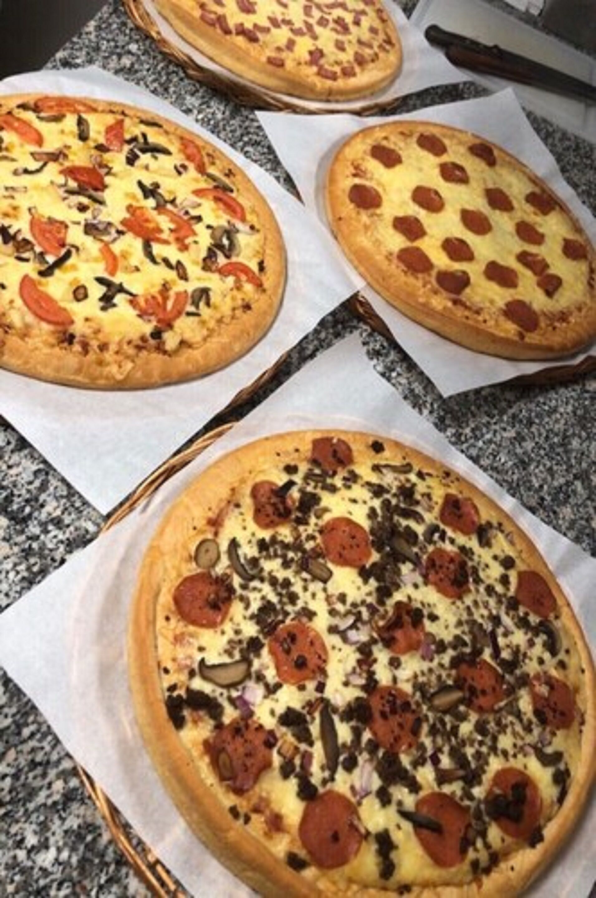 Tres pizzas sobre una encimera de granito.