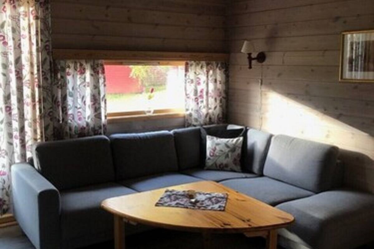 A cozy room with a grey sectional sofa, a wooden coffee table, and a window with floral curtains.