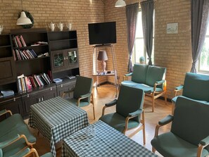 A cozy living room with a brick wall, a flat-screen TV, a bookshelf, and a dining area with checkered tablecloths. - Femo Kro & Feriecenter by DanCenter (Maribo)