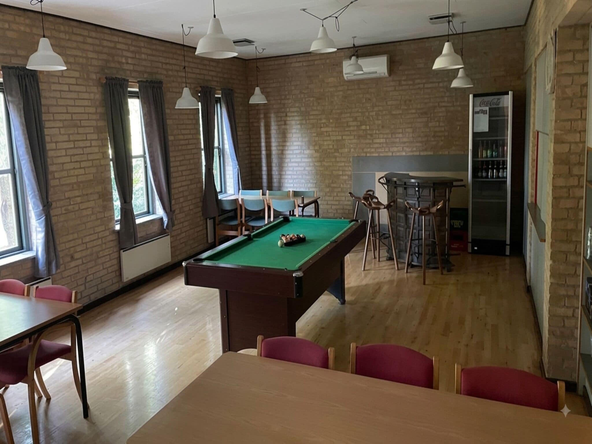 Uma sala com mesa de bilhar, cadeiras, bar e parede de tijolos.