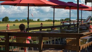 A deck with outdoor seating, red umbrellas, and a view of the sea and airplanes in the background. - Femo Kro & Feriecenter by DanCenter (Maribo)