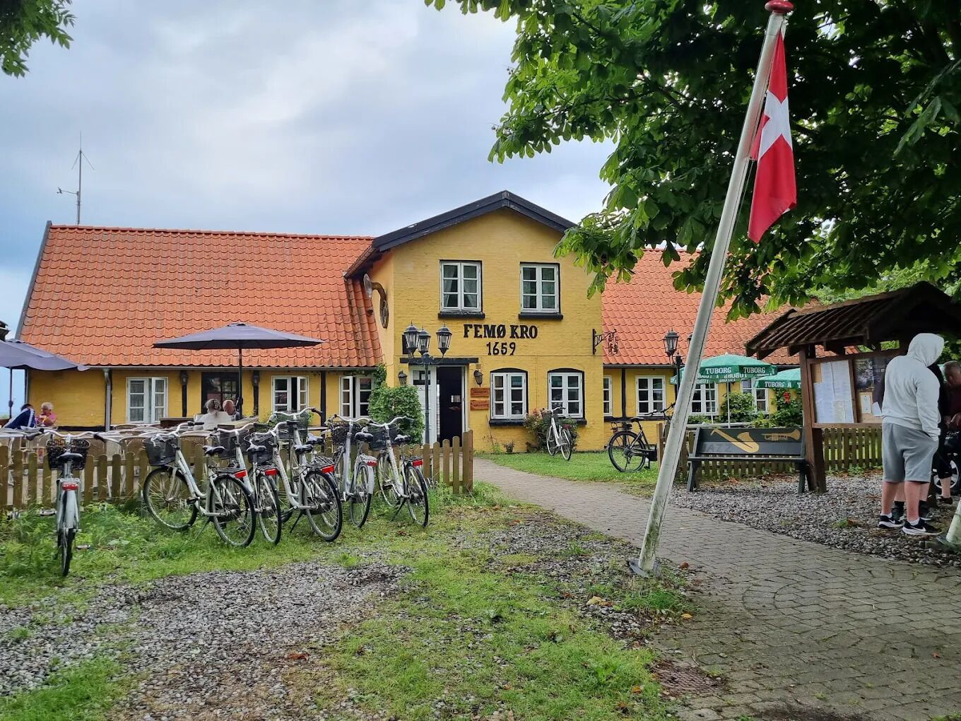 A yellow building with a red-tiled roof, a flag, and bicycles parked outside.