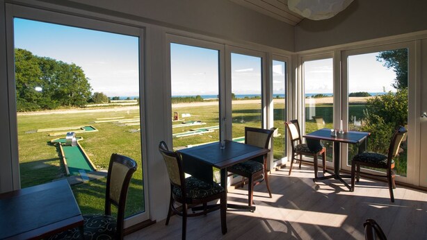 A sunlit room with large windows overlooking a grassy area and a pool. - Femo Kro & Feriecenter by DanCenter (Maribo)