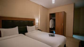 A hotel room with two beds, a wooden wardrobe, and a small desk with a laptop.